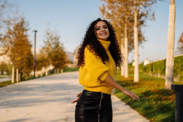 Hojas amarillas del parque y armonizando con ellas suéter amarillo belleza rizada morena caminando o