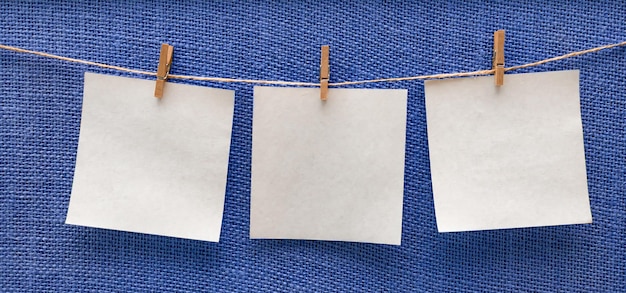 Hojas blancas de papel colgando aisladas en un tablero azul beige en una maqueta de espacio libre de pinzas para la ropa