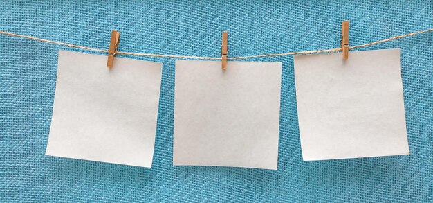 Hojas blancas de papel colgando aisladas en un tablero azul beige en una maqueta de espacio libre de pinzas para la ropa