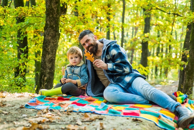 Hojas caídas. Papá barbudo hipster con lindo hijo pasan tiempo juntos en el bosque. Tiempo familiar. Ocio familiar. El hombre barbudo brutal y el niño disfrutan de la naturaleza otoñal. Valores familiares. Concepto de pasión por los viajes