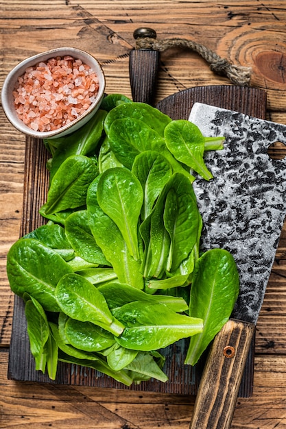 Hojas de ensalada verde de bebé romain sobre tabla de cortar de madera.