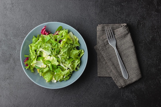 Hojas de ensalada verde en un cuenco sobre una mesa negra.