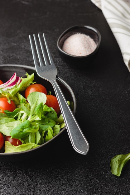 Hojas de ensalada verde con tomates cherry en un tazón sobre mesa negra