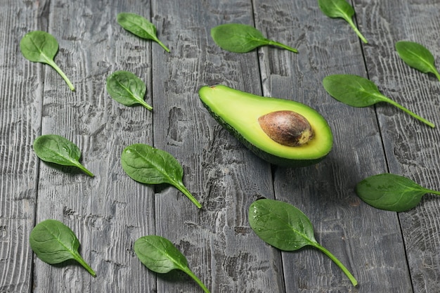 Hojas de espinaca esparcidas y medio aguacate sobre una mesa de madera negra. Ingredientes para la bebida y la ensalada.