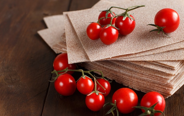 Hojas de lasaña cruda y tomates cherry en una mesa de madera