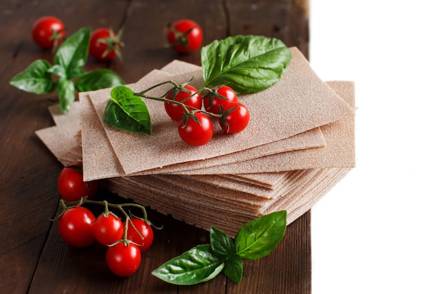 Hojas de lasaña cruda y tomates cherry en una mesa de madera