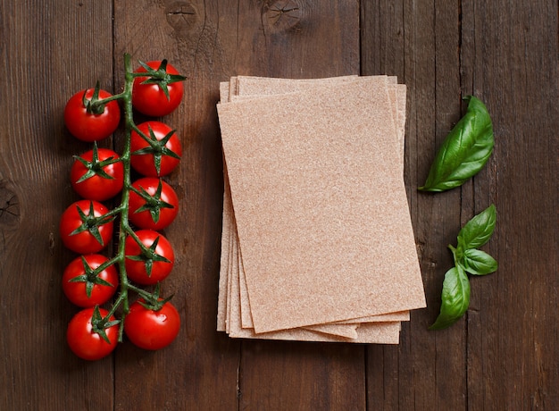 Hojas de lasaña de trigo integral, tomates y albahaca sobre mesa de madera