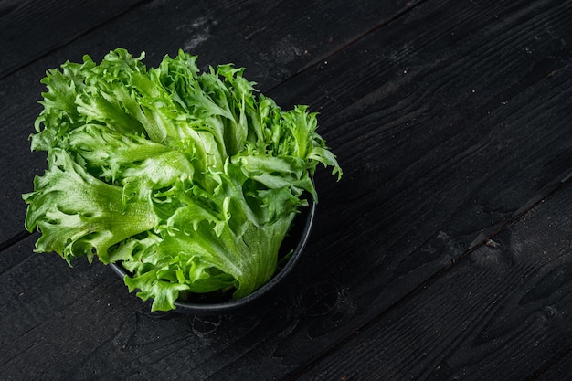 Hojas de lechuga batavia verde orgánica fresca, sobre fondo de mesa de madera negra con espacio para copiar texto