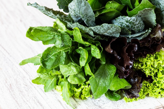 Hojas de lechuga verde y roja, rúcula, col rizada, amaranto, espinacas en mesa blanca