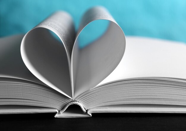 Hojas de libro curvadas en forma de corazón sobre fondo azul desenfocado