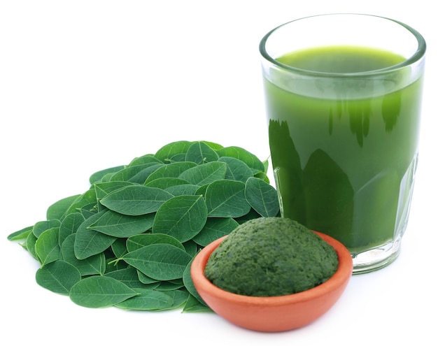 Hojas de moringa comestible con extracto y pasta molida sobre fondo blanco.