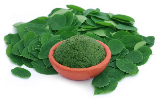 Hojas de moringa comestible con pasta molida en una alfarería sobre fondo blanco.