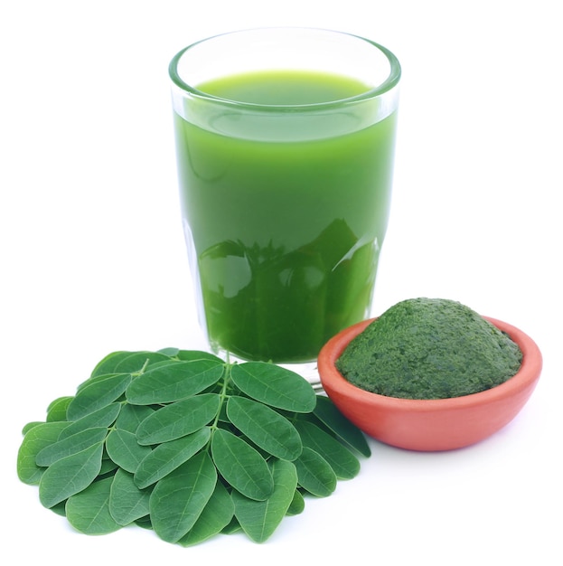 Hojas de Moringa con extracto en un vaso sobre fondo blanco.