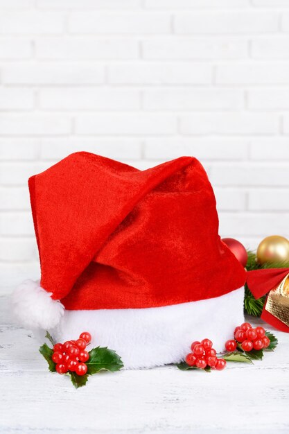 Hojas de muérdago con sombrero de Navidad en la mesa sobre fondo de pared de ladrillo