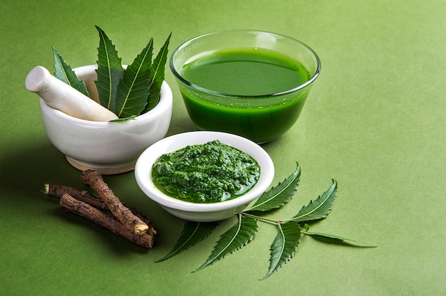 Hojas de neem medicinales en mortero y mortero con pasta de neem, jugo y ramitas