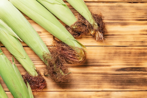 Las hojas de la oreja de la mazorca de maíz de leche verde dulce y fresca se encuentran sobre el fondo de la mesa de madera quemada marrón Lay plano Vista superior Espacio de copia