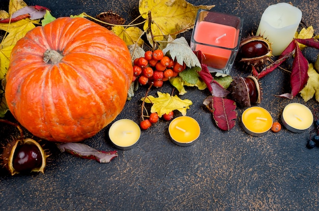 Hojas de otoño, calabaza, castañas, velas sobre un fondo oscuro