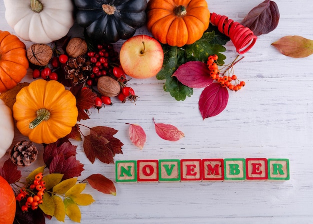 Hojas de otoño y calabazas con texto noviembre sobre fondo de madera