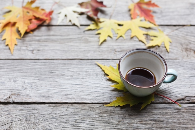 Hojas de otoño y composición de café negro. Taza de café azul medio vacía en la mesa de madera rústica desgastada. Concepto de bebidas calientes de otoño