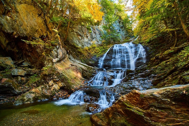 Las hojas de otoño cubren el desfiladero rocoso con una cascada furiosa y árboles en el follaje máximo