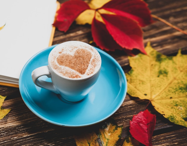Hojas del otoño, libro y taza de café en la tabla de madera.