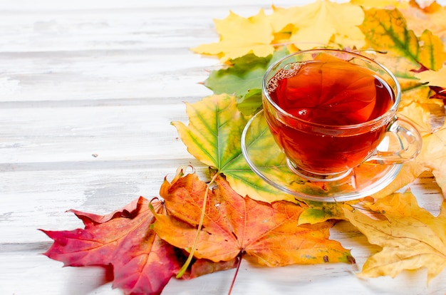 Hojas de otoño y taza de té en la mesa de madera