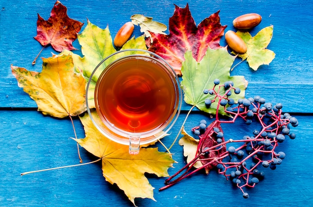 Hojas de otoño y taza de té en la mesa de madera