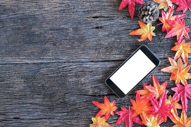 Foto hojas de otoño y teléfono móvil de la maqueta en fondo de madera de la naturaleza con el espacio de la copia.