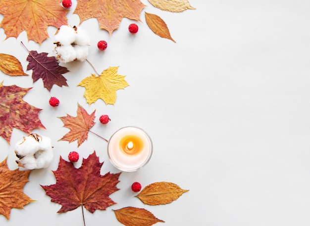 Hojas de otoño y velas sobre fondo blanco.