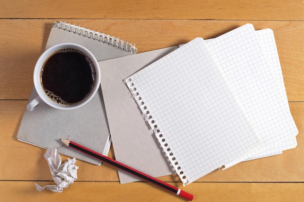 Hojas de papel en blanco de un lápiz de cuaderno y papel arrugado en un escritorio de madera con vista superior de la taza de café