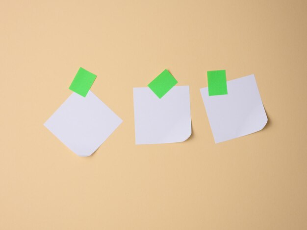 Hojas de papel cuadradas blancas pegadas con papel adhesivo verde sobre un fondo marrón claro