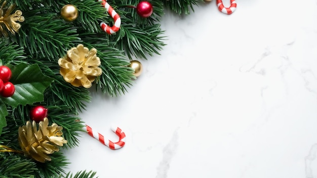 Hojas de pino verde, adornos navideños rojos y bastones de caramelo sobre fondo de mármol blanco, adornos navideños en color rojo brillante. Concepto de navidad simple y creativo.