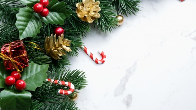 Hojas de pino verde, adornos navideños rojos y bastones de caramelo sobre fondo de mármol blanco, adornos navideños en color rojo brillante. Concepto de navidad simple y creativo.