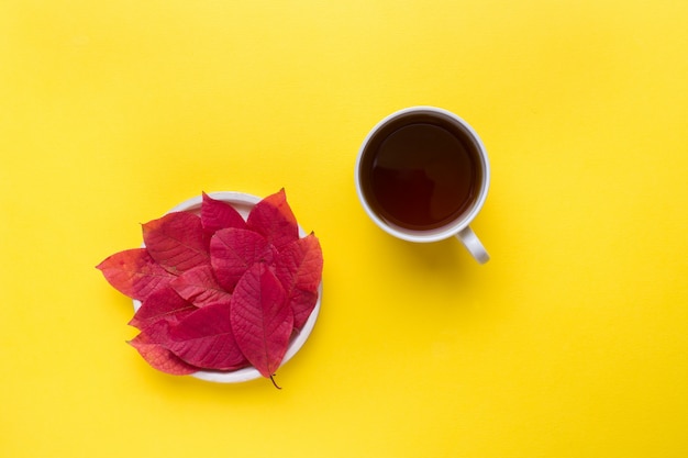 Hojas rojas de otoño y una taza de café sobre un fondo amarillo brillante