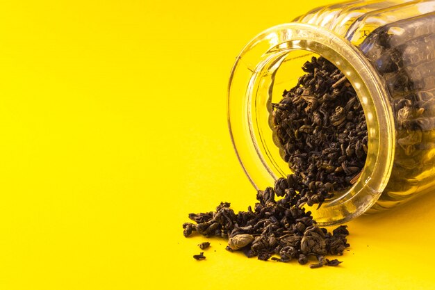 Hojas secas de té negro en vidrio sobre fondo amarillo