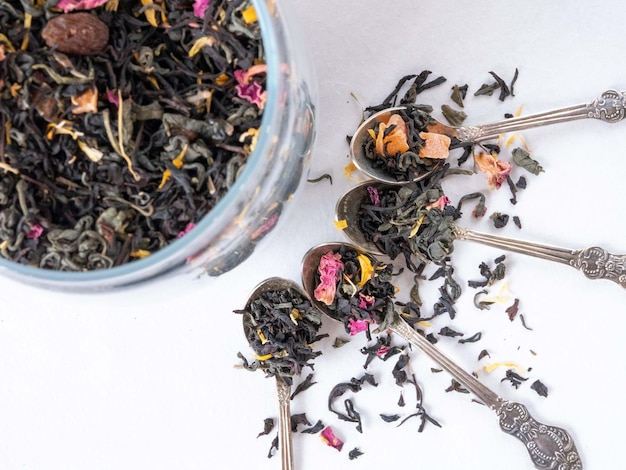 Las hojas secas de té se vierten en hermosas cucharas Té negro con sabor a hierbas medicinales en un frasco de vidrio El té se rocía sobre la mesa Bebida calmante Concepto de tienda de té