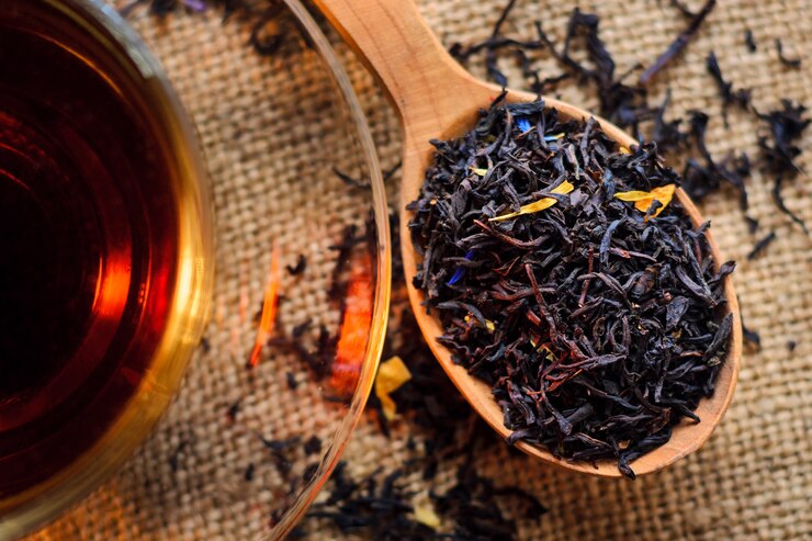 Hojas de té en una cuchara de madera junto a una taza de té hecho en un fondo de arpillera