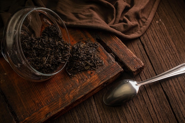 Hojas de té verde en un frasco de vidrio con una cuchara en una tabla marrón de madera sobre un fondo oscuro tiempo de preparación del té