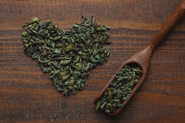 Hojas de té verde secas en forma de corazón y cuchara sobre un fondo de madera