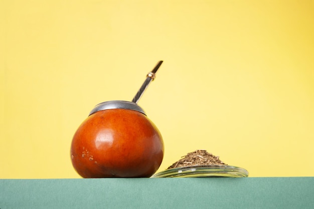 Hojas de té de yerba bombilla mate en un podio verde sobre un fondo amarillo