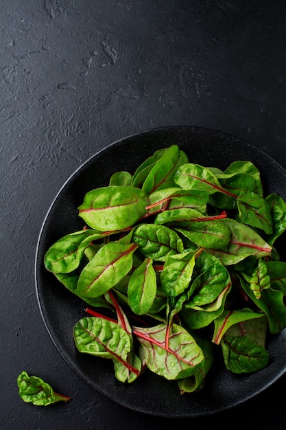 Hojas tiernas de acelga para ensalada en un plato de cerámica oscura sobre hormigón negro.