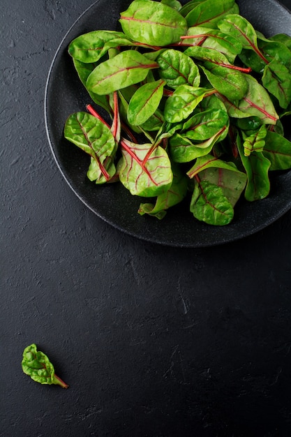 Hojas tiernas de acelga para ensalada en un plato de cerámica oscura sobre hormigón negro.