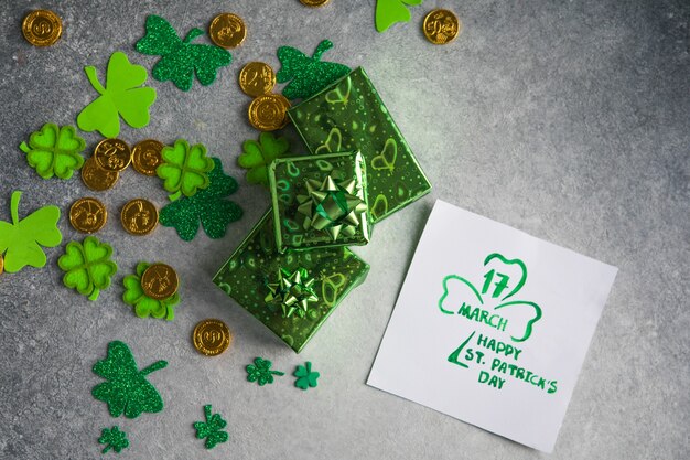 Hojas de trébol decorativo, caja de regalos verde, monedas sobre fondo de piedra, plano laical. Celebración del día de San Patricio. Tarjeta feliz día de San Patricio