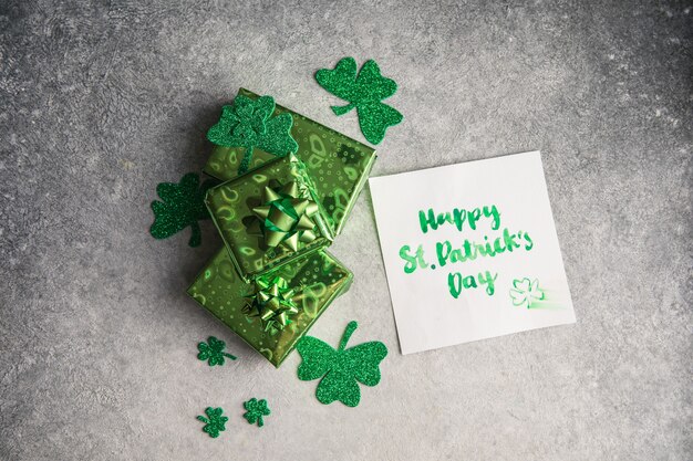 Hojas de trébol decorativo, caja de regalos verde, monedas sobre fondo de piedra, plano laical. Celebración del día de San Patricio. Tarjeta feliz día de San Patricio