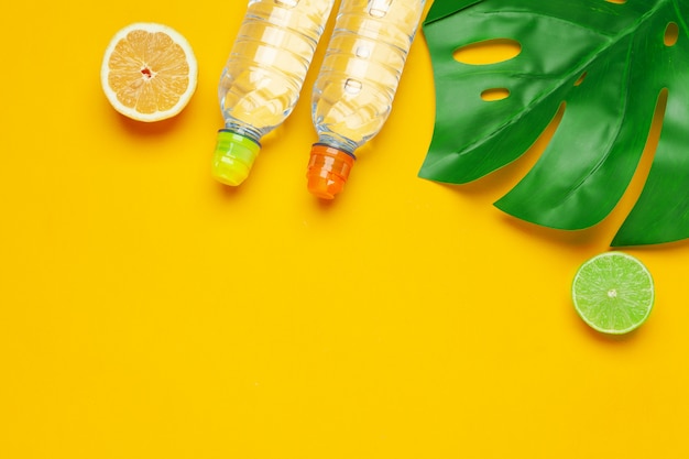 Hojas tropicales y botella de agua sobre fondo amarillo. Fruta de desintoxicación de agua infundida.