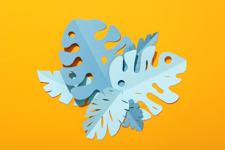 Hojas tropicales de papel azul sobre un fondo amarillo.