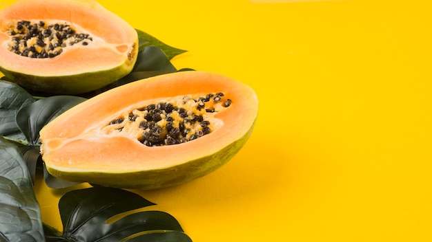 Foto hojas verdes artificiales con fruta de papaya a la mitad sobre fondo amarillo