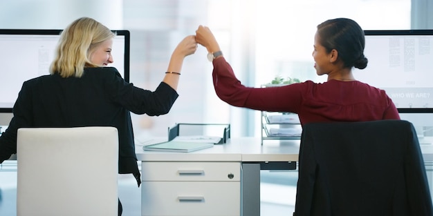 Hoje nos superamos Foto retrospectiva de duas jovens empresárias batendo os punhos em sucessão enquanto estavam sentadas em sua mesa no escritório