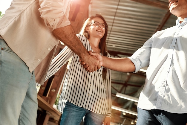 Hola dos hombres dándose la mano y sonriendo mientras están de pie con sus compañeros de trabajo en la oficina moderna