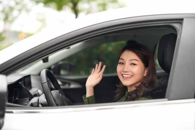 ¡Hola! Hermosa joven alegre mirando a la cámara con una sonrisa y saludando mientras está sentado en su coche